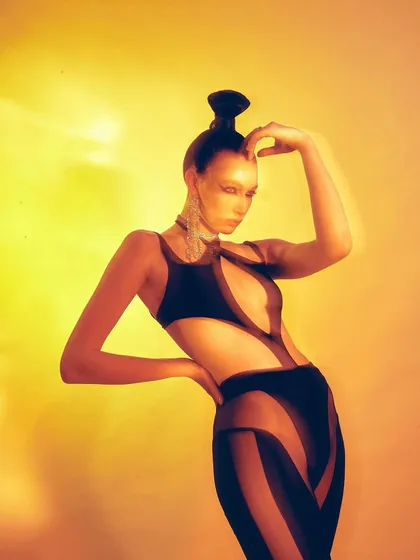 A motion-blur shot from the Mugler x H&M editorial, conveying energy and movement. The styling with the sleek updo and cut-out bodysuit creates a futuristic, almost sci-fi aesthetic.