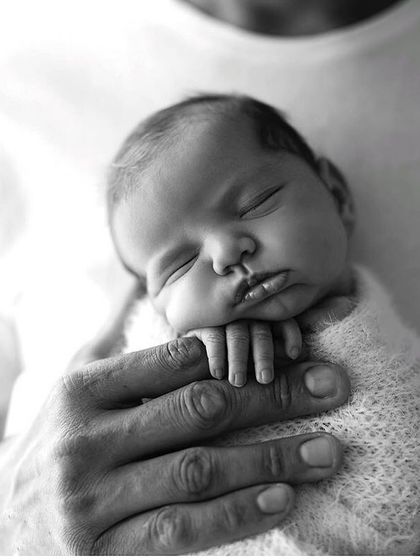 The comfort of a parent's touch. This image showcases the gentle and secure way we handle newborns, capturing a moment of pure peace and trust.