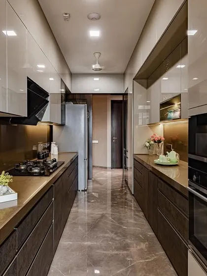 A long galley kitchen with dark wood-textured lower cabinets and glossy beige upper cabinets. The marble flooring and warm lighting create a luxurious and inviting atmosphere.