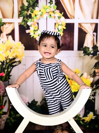 A happy baby girl in a vibrant floral market setup, smiling brightly.