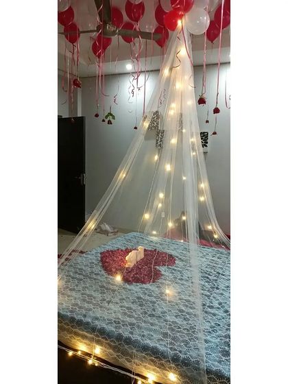 A focused shot of the fairy light canopy over the bed. A heart made of rose petals and a lit "LOVE" sign are placed on the bed as a centerpiece for this first-night decor.