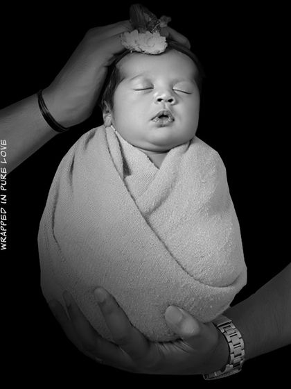 A symbolic black and white image of parents' hands holding their swaddled baby. This artistic shot represents the pure love and protection surrounding their new child.