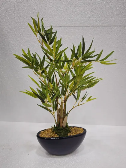 A small artificial bamboo plant in a dark bowl, perfect for adding a touch of zen to a desktop.