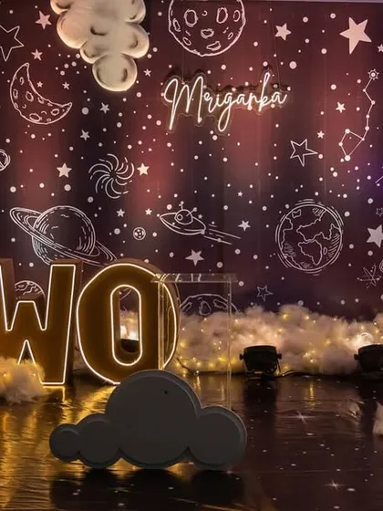 A spectacular 'Two The Moon' space-themed 2nd birthday party. The backdrop features a galaxy print, light-up letters, a moon prop, and fluffy clouds, creating a universe of fun for the little one.