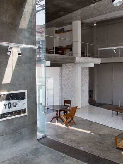 The interior of the Artrovert studio, featuring raw concrete surfaces, double-height volumes, and a mezzanine study. The space is designed to be rugged, flexible, and filled with natural light.