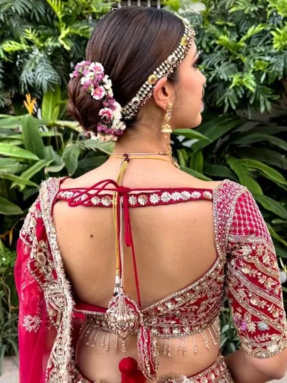 A back view of a sleek bridal bun adorned with a semi-circle of fresh pink and white flowers. This is a perfect example of a classic floral bun for a wedding ceremony.