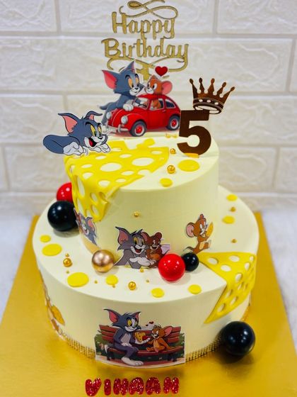 A playful Tom and Jerry cake for a 5th birthday. This two-tiered cake features the classic chase with cheese-themed details and fun scenes from the beloved cartoon.