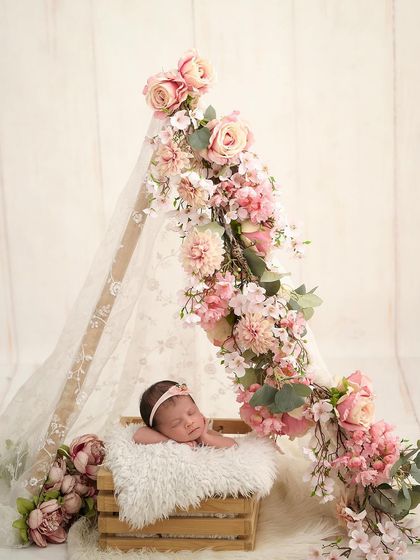 A tiny newborn sleeps in a wooden crate inside a lace teepee, which is beautifully decorated with a cascade of pink flowers for a boho-chic look.