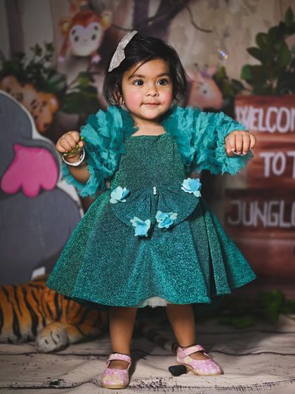 A full-length view of this beautiful teal party dress, showing off the ruffled sleeves and floral details against the jungle backdrop.