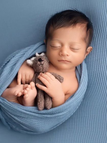 This little boy is snuggling his teddy bear while wrapped in a soft blue swaddle. It's a classic pose that shows their tiny size and peaceful nature.