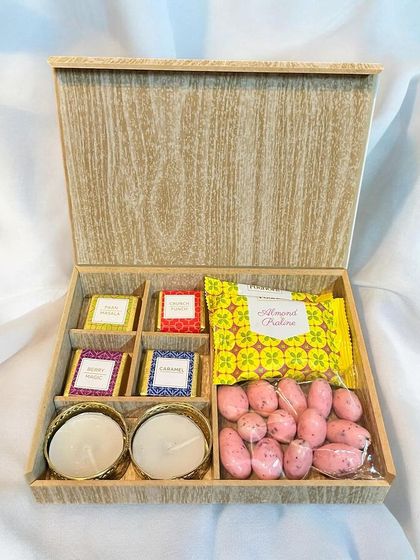 This wooden gift box is filled with a curated selection of Diwali treats, including strawberry-coated almonds, assorted chocolates, and traditional diyas for the festival of lights.