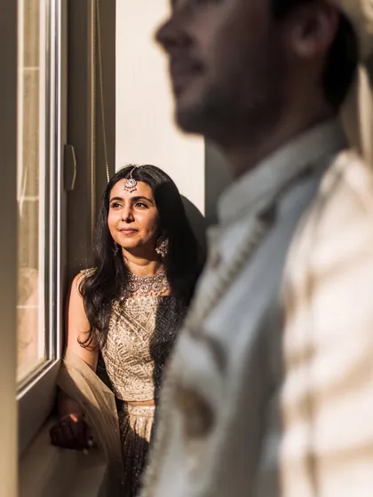 An artistic shot using natural window light. The bride looks out thoughtfully while the groom is softly focused in the foreground, creating a sense of anticipation.