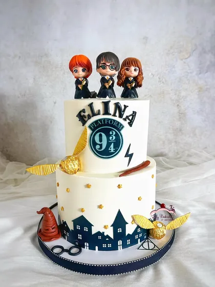 Calling all Potterheads! This magical two-tier Harry Potter cake features the iconic Platform 9 3/4, the golden snitch, and the sorting hat. It's a buttercream cake, showing that you don't need fondant for a detailed theme.