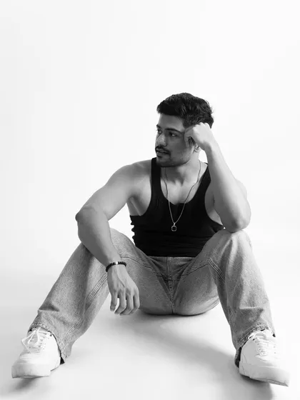 A thoughtful black and white studio portrait. The simple tank top and jeans combination keeps the focus on the model's physique and expression.