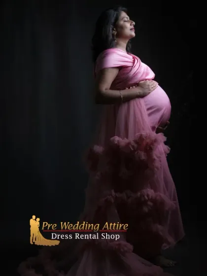 A dramatic studio portrait in our dusty pink ruffled gown. The side profile and focused lighting beautifully highlight the baby bump and the intricate texture of the satin bodice and tulle skirt.