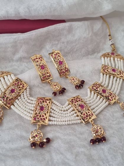 The complete 'Apsara' set in a rich ruby red. This Hyderabadi choker, with its multi-strand pearl detailing and matching earrings, is a classic choice for weddings and festive events.
