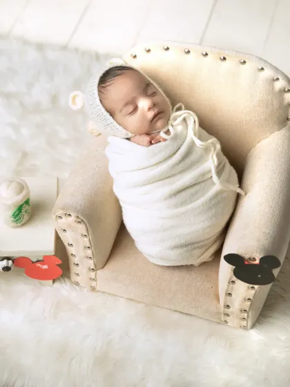 A wider shot of the swaddled baby in the armchair, showing a hint of a Mickey Mouse theme with the garland in the foreground.