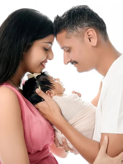 A classic newborn and family portrait against a clean, white background. The parents' heads are touching as they hold their baby, creating a strong triangular composition that symbolizes family unity.
