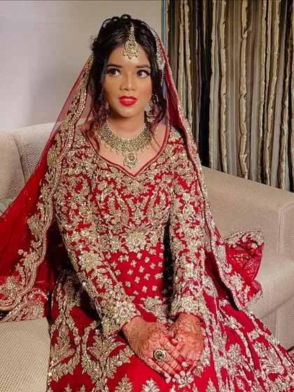 The bride seated, looking like royalty in her magnificent red and gold embroidered wedding attire.