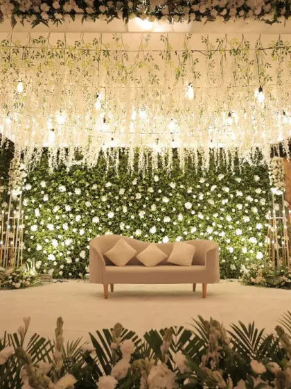 A straight-on shot of the elegant white floral stage, emphasizing the dense flower wall and the delicate hanging floral ceiling. This view showcases the sheer volume and artistry of the floral work involved.