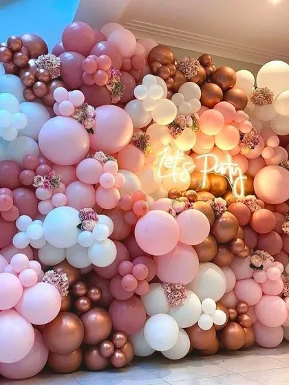 A full wall of pink and rose gold balloons with a 'Let's Party' neon sign, creating an immersive and festive photo backdrop.