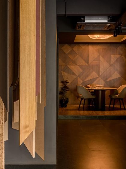 The design uses layers to create intrigue, with the hanging veneer panels partially obscuring the view into the discussion room.