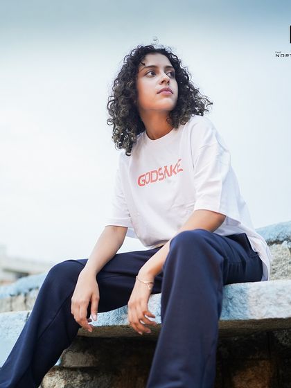 A model wearing the white Godsake graphic tee. The oversized fit provides a comfortable and stylish drape, perfect for a relaxed look.