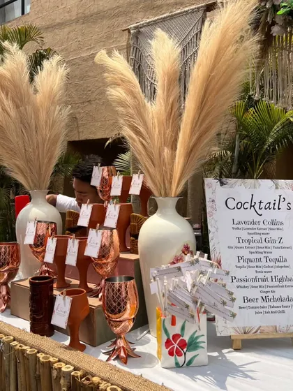 A beautiful bohemian bar setup, featuring pampas grass, copper pineapple mugs, and a custom cocktail menu with drinks like 'Lavender Collins' and 'Tropical Gin Z'.