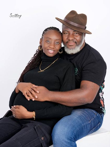 A happy and relaxed couple portrait in a high-key studio setting. Their casual black outfits and joyful interaction create a natural and heartwarming image.
