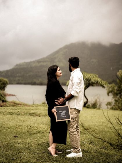 A stunning wide shot of the couple by a lake, with a mountain in the background. They are holding an announcement sign, but the focus is on their connection in the majestic landscape.