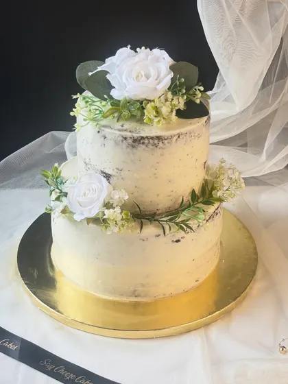 For those who love understated elegance, I design rustic semi-naked cakes. This two-tier cake features a light layer of buttercream and is decorated with carefully selected, food-safe artificial white blooms and greenery for a minimalist yet charming look.