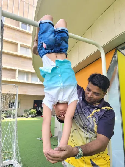 A student performs an inverted hang with the assistance of a coach, demonstrating the advanced skills and trust built during our gymnastics program at the summer camp.