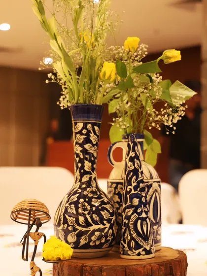 A close-up of the table decor, featuring hand-painted blue pottery vases filled with yellow flowers, adding a touch of artisanal charm to the Haldi celebration.