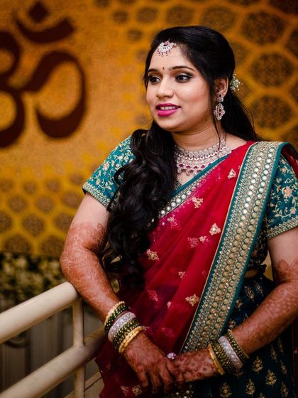 This bride's reception style is both elegant and modern. Her side-swept hair, diamond jewelry, and glowing makeup create a sophisticated look against the backdrop of the 'Om' symbol.
