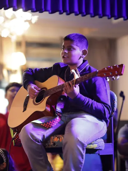 A young student confidently strums his acoustic guitar on stage. The annual showcase is a huge confidence booster for our performers.
