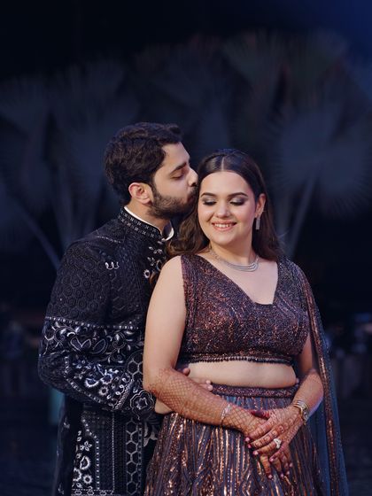 An intimate portrait from the sangeet night. The groom gently kisses the bride's forehead as she smiles, a perfect capture of their affection.