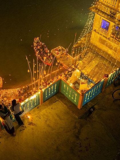 A closer drone view of a decorated ghat during Dev Deepawali. This shot focuses on the intimate details of the celebration, with families lighting diyas by the water's edge.