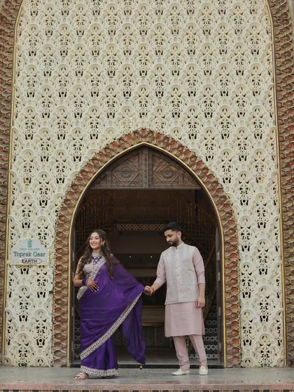 A playful and dynamic portrait of Devanshi and Anshul. Her leading him by the hand adds a sense of movement and joy, set against an intricately detailed wall that adds texture and grandeur.