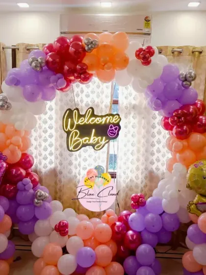 A 'Welcome Baby' ring decoration in pastel shades of purple, orange, and pink. This setup includes a neon sign and cute baby-themed foil balloons.