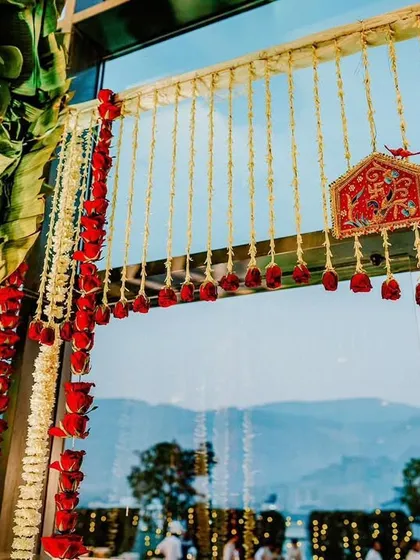 A detail of a minimal mandap entrance, with hanging garlands of mogra and red roses, and a small Ganesha idol for blessings.