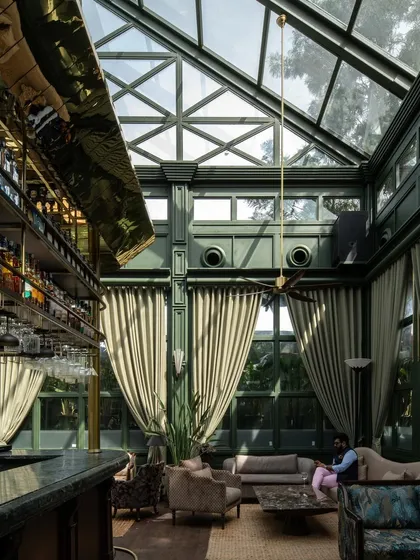 The grand, double-height interior, where a brass-clad bar canopy reflects the light from the glass ceiling. The scale is dramatic, yet the seating arrangements create intimate, comfortable zones.