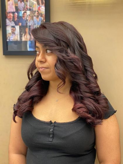 A side profile of a client with a rich, wine-colored hairstyle. The voluminous curls add a touch of old-hollywood glamour to this bold and confident look.