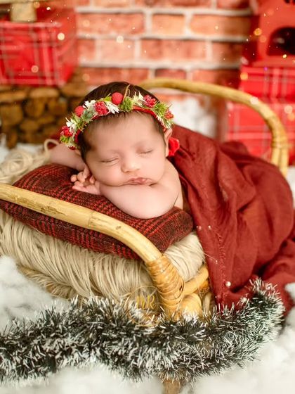 A sleeping newborn wearing a festive floral headband, nestled in a sleigh prop for a Christmas-themed photoshoot.