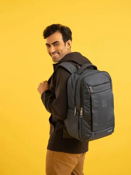 A man smiling as he looks back, wearing a practical and sleek backpack against a bright yellow background. This shot is friendly and approachable, highlighting the bag's suitability for daily commutes or travel.