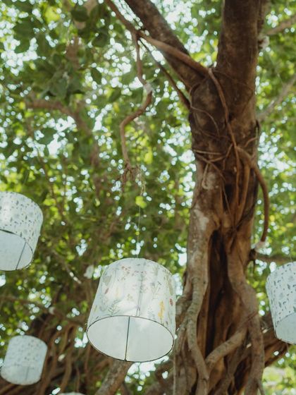 Custom-printed lampshades hanging from the trees, adding a whimsical and artistic touch to the outdoor Mehendi decor in Goa.