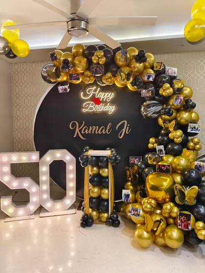 A personalized 50th birthday decoration in a striking black and gold theme. The balloon arch is customized with small photos of the celebrant, creating a beautiful memory wall, alongside large light-up '50' marquee numbers.