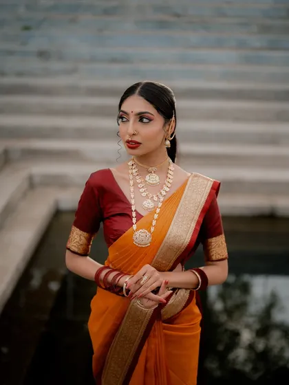A three-quarter shot that focuses on the details of the saree and the layered necklaces. The soft lighting and the model's pose create a feeling of timeless grace.