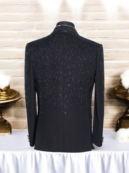 This image displays the back of a custom black tuxedo jacket, highlighting the intricate sequin and beadwork that flows down the upper back and sleeves. This detail ensures the garment is impressive from every angle.