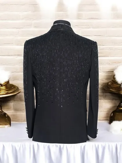 This image displays the back of a custom black tuxedo jacket, highlighting the intricate sequin and beadwork that flows down the upper back and sleeves. This detail ensures the garment is impressive from every angle.