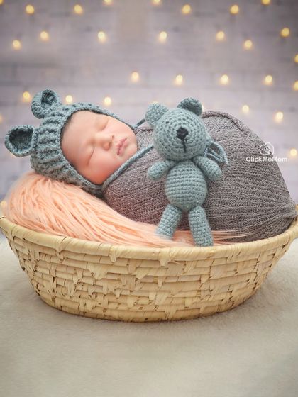 This little one is sleeping soundly with his teddy bear friend in a simple wicker basket, wearing an adorable knitted bear hat.